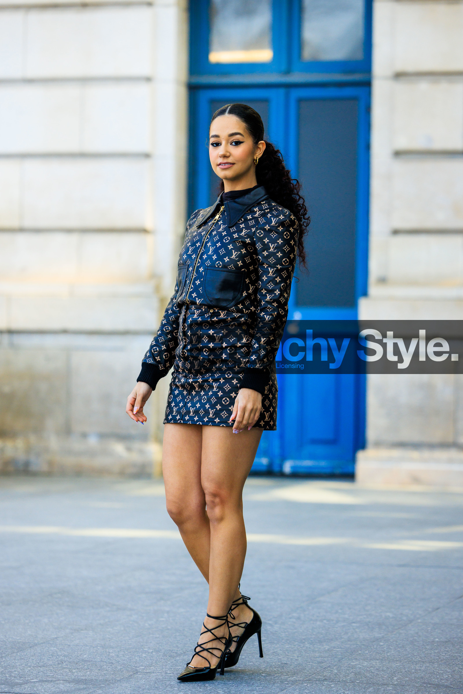 louis vuitton, curly hair, pony tail, louis vuitton set, monogram set, logo skirt, logo jacket, printed jacket, printed skirt, mini skirt, black top, black sandals, laced sandals, monogram skirt, cat eye, make upmonogram jacket, golden loops, lena mahfouf, street style, jonathan paciullo, FW, frenchystyle, fashion week, AUTUMN WINTER 2022-2023, FALL WINTER 2022_2023, FW 22-23, PFW, PARIS, full length, vertical